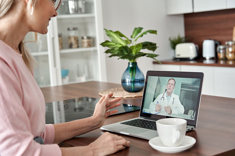 Middle-aged female patient receiving online telemedicine consultation at home via telehealth video call on a laptop computer using high speed fibre internet